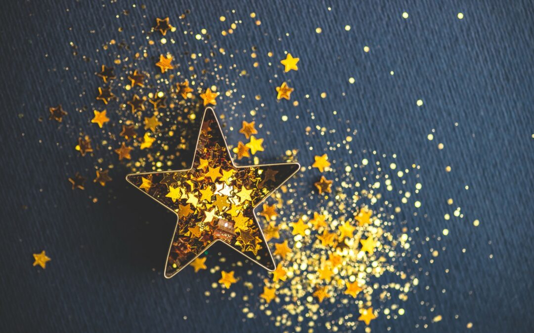 A star-shaped cookie cutter laying on a grey background, filled with gold star confetti