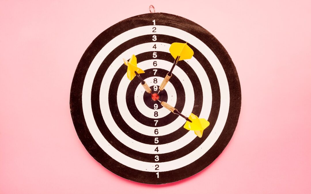 A red and white stripped bullseye with three arrows in the center, laying on a pink background.